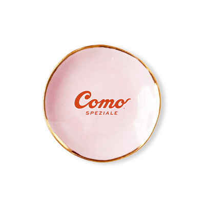 A small round light pink ceramic tray with a gold rim and the red text 'Como SPEZIALE' printed in the center, shown on a plain white background.