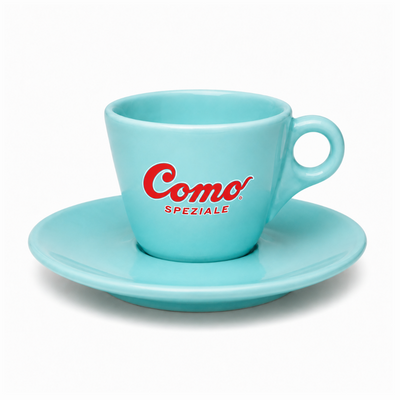 A light turquoise blue ceramic espresso cup with a matching saucer, featuring the red 'Como Speziale' logo on the front, set against a clean white background.