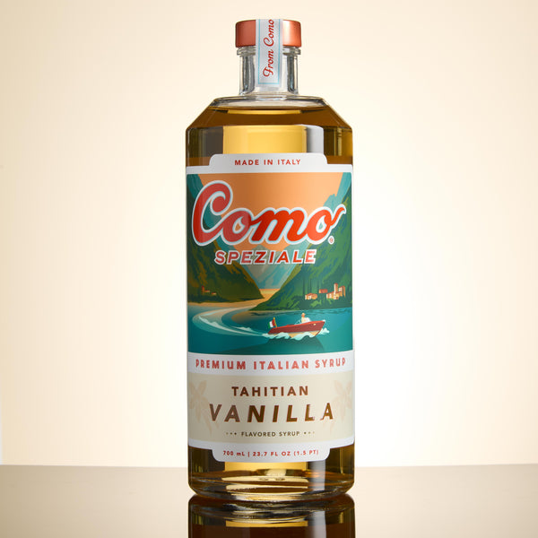 A bottle of Como Speziale Tahitian Vanilla premium Italian syrup, featuring a colorful scenic label and a copper-colored cap, set against a clean beige background.