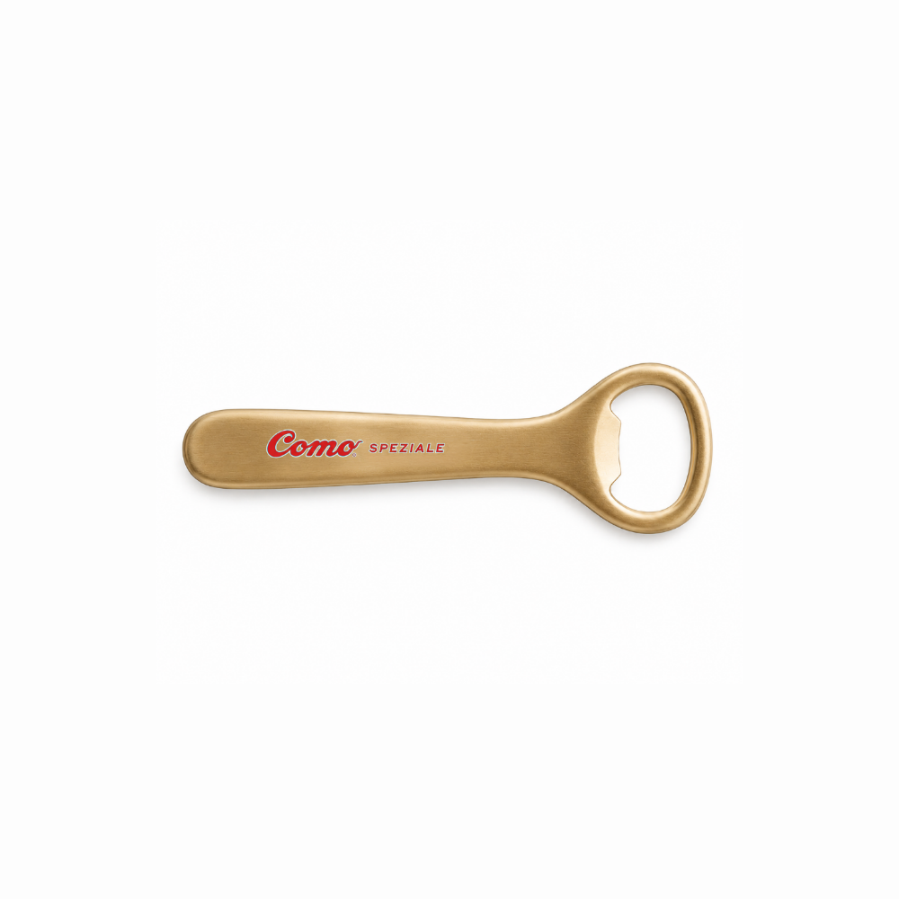 A gold-colored metal bottle opener with 'Cosmo SPEZIALE' printed in red on the handle, set against a plain white background.