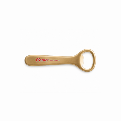 A gold-colored metal bottle opener with 'Cosmo SPEZIALE' printed in red on the handle, set against a plain white background.
